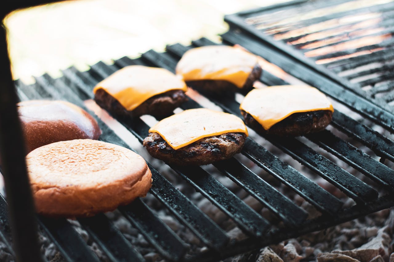 Juicy cheeseburgers and buns grilling on a charcoal barbecue outdoors.