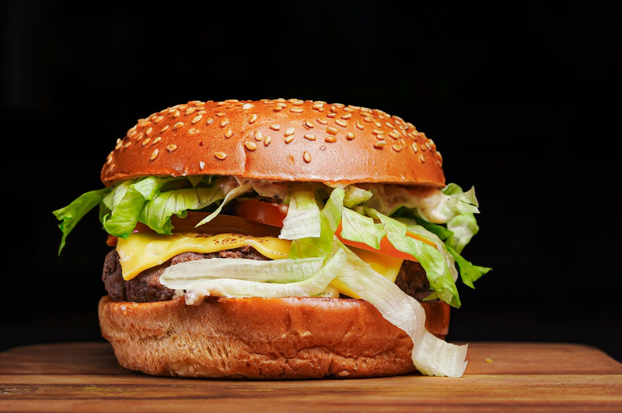 Close-up of a juicy cheeseburger with lettuce, tomato, and cheese in a sesame seed bun.